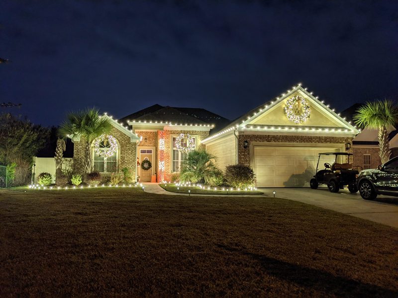 Home with warm white roofline lights, a lit wreath and wrapped palms