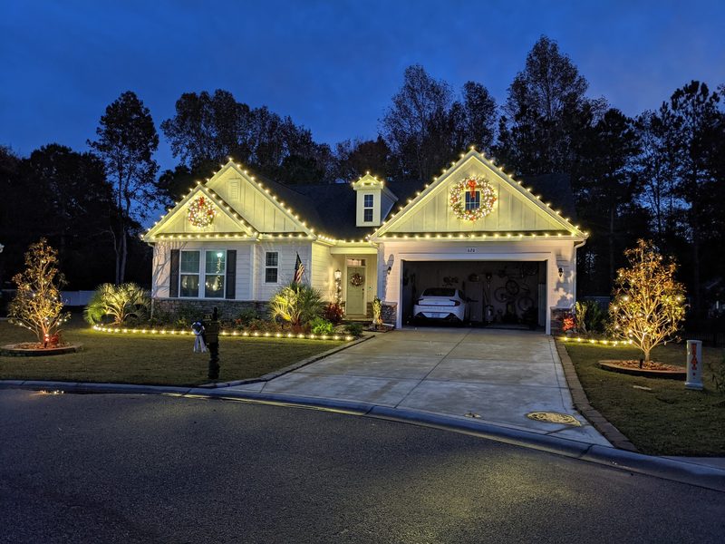 Two-story home with warm white roofline lights, a lit wreath and a lit garage